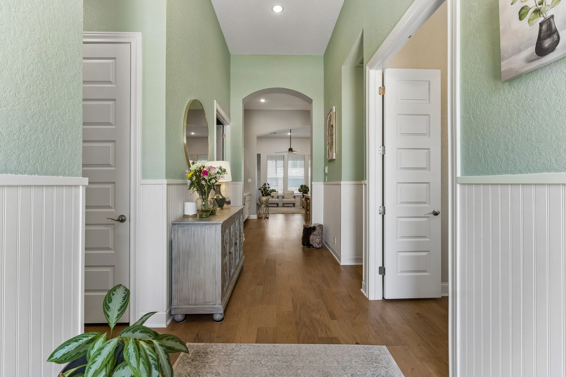 Sage-walled entry hall with white wainscoting and an arch leading toward the living room