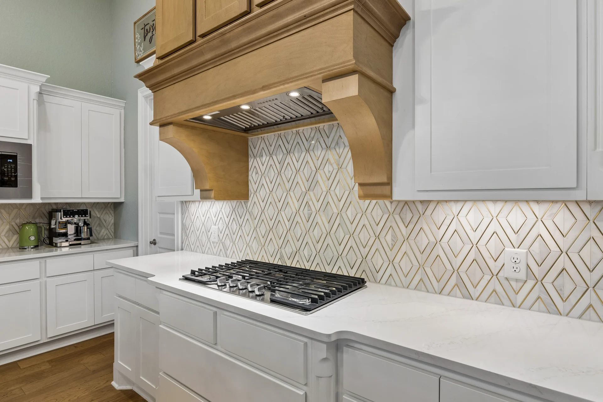 Gas cooktop beneath the wood range hood and geometric backsplash