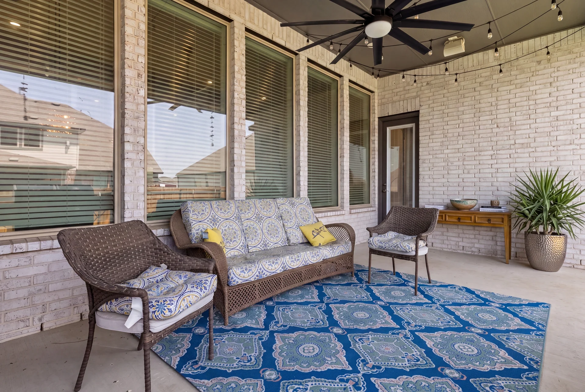 Covered white-brick patio with sofa, chairs and blue rug